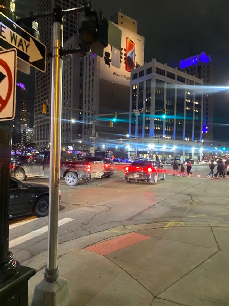 a busy city street at night with cars and people walking on the sidewalk, traffic lights in the background