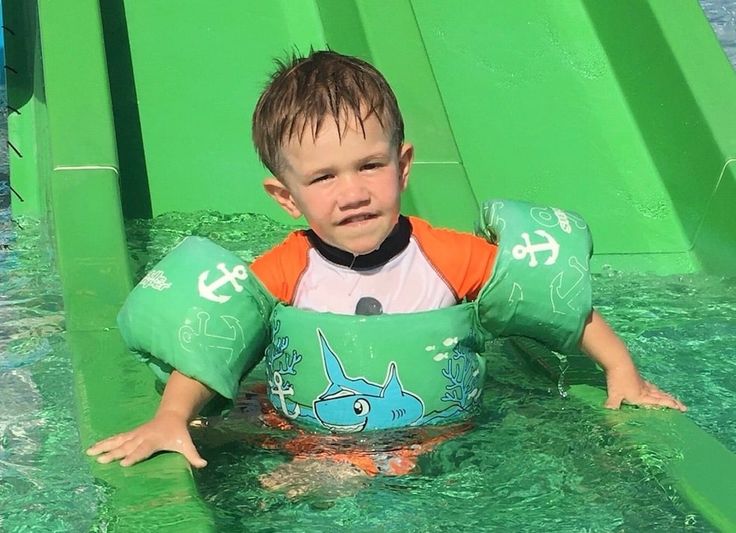 a young boy riding on top of a green slide in the water at a park