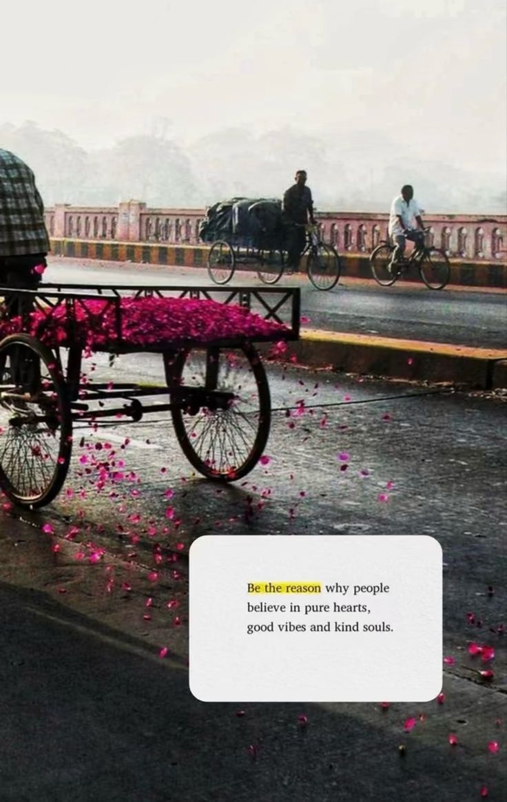 two people riding on a cart with pink flowers in the back and one person pushing a bicycle behind them