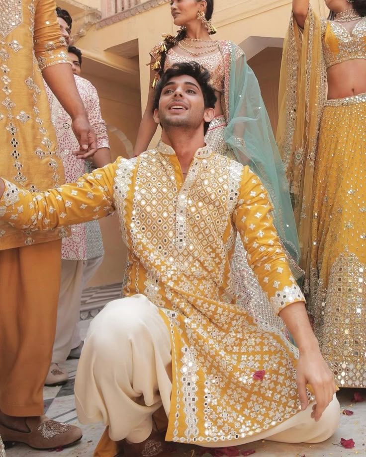 a man kneeling down in front of some other people wearing yellow and white attires