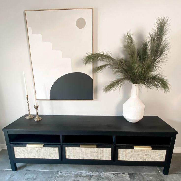 a black table with two baskets and a vase on it next to a plant in a white vase