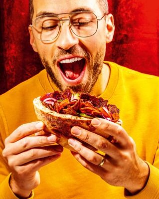 a man with glasses eating a sandwich in front of his face and mouth wide open