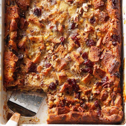 a casserole dish with bread and cranberries in it next to a spatula