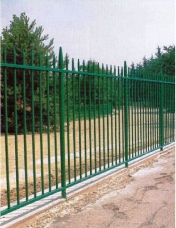 a green metal fence next to a dirt road with trees in the backgroud