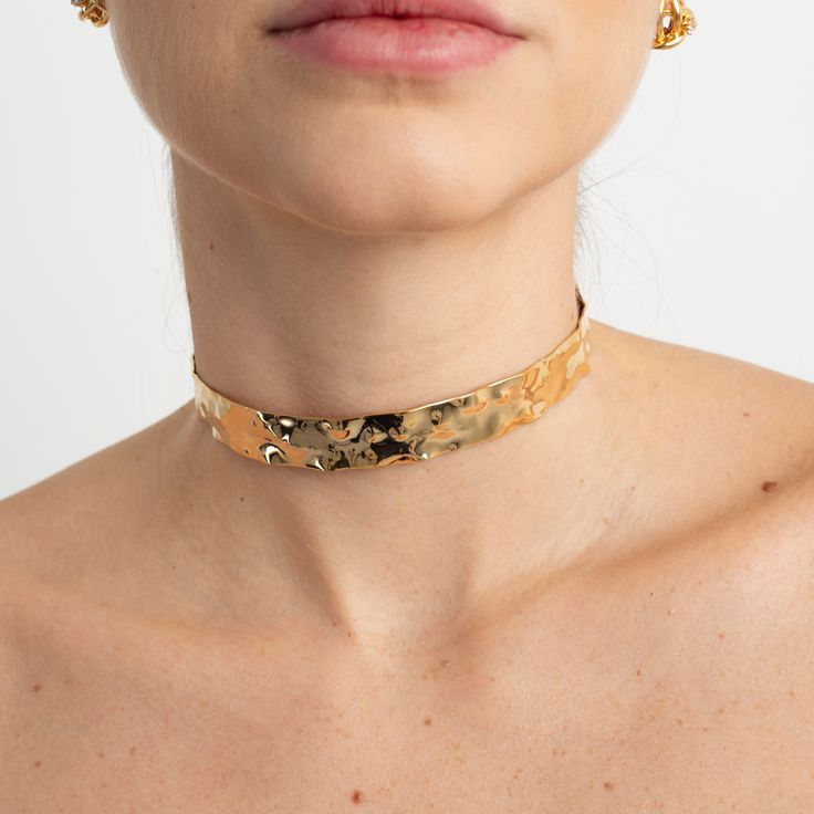 The Natasha Choker is a stunning piece that combines contemporary style with sophistication. Its noble metal structure features a hammered design, adding unique texture and elegance to the accessory. With gold plating, this choker exudes luxury and durability. Measuring 10 x 10 cm, the Natasha Choker makes a bold statement, sure to attract attention at any occasion. **Details:** - Material: Noble metal- Plating: Gold- Hammered design- Size: 10 x 10 cm Elegant Hammered Choker Jewelry, Elegant Hammered Choker Necklace, Hammered Metal Choker Necklaces, Metal Hammered Choker Necklace, Adjustable Gold Choker Tarnish Resistant, Gold Plated Choker For Party, Gold Plated Gold Choker For Party, Modern Gold Choker For Party, Formal Brass Choker