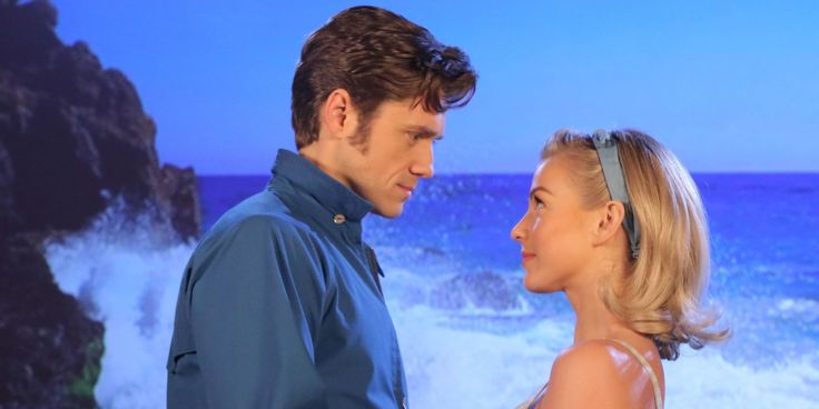 a man and woman standing next to each other in front of the ocean with waves