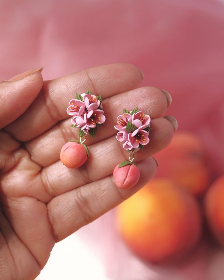 a hand holding two small pink flowers on top of it's earring posts