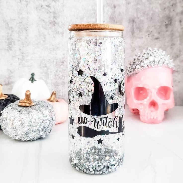 a glittered tumbler with the words bad witch on it next to skulls and pumpkins