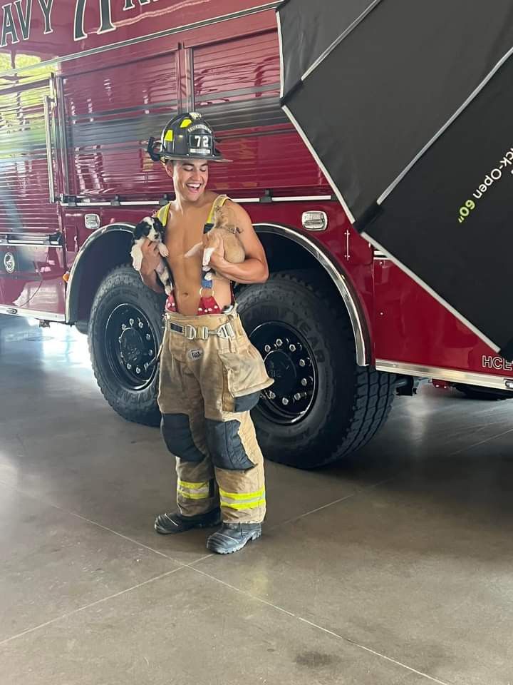 a fireman standing in front of a large truck with his shirt off and helmet on