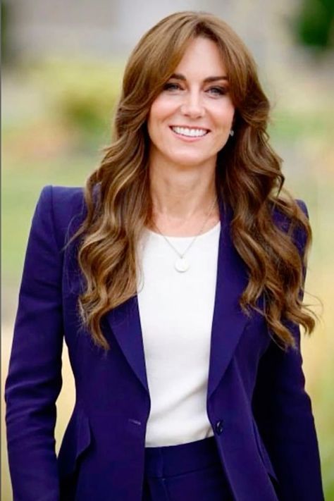 a woman with long hair wearing a blue jacket and white top smiles at the camera