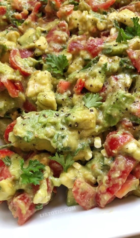 a white plate topped with guacamole covered in tomatoes and cilantro