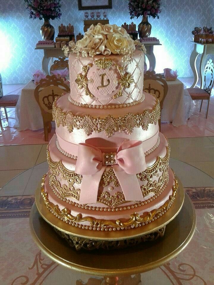 a three tiered cake is adorned with pink and gold ribbons, roses, and monograms