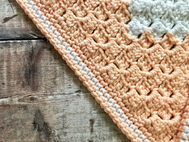 an orange and white crocheted blanket laying on top of a wooden floor next to a piece of wood