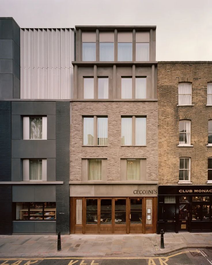 the corner of two buildings in front of each other on a city street with cars parked nearby