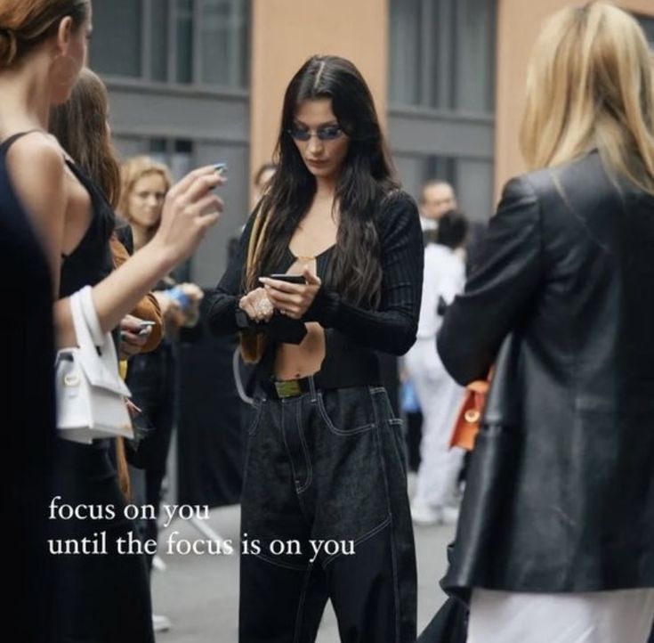 a woman standing on the street looking at her cell phone with people in the background