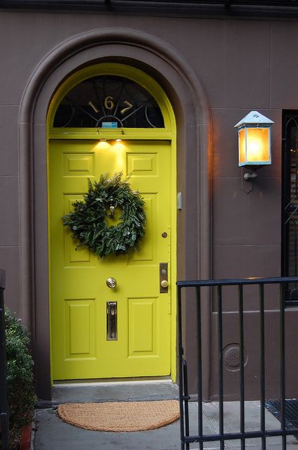 a yellow front door with a wreath on it and a black gate in front of it