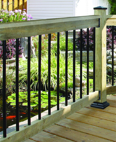 a wooden deck with black iron railings and plants on the other side, in front of a white house