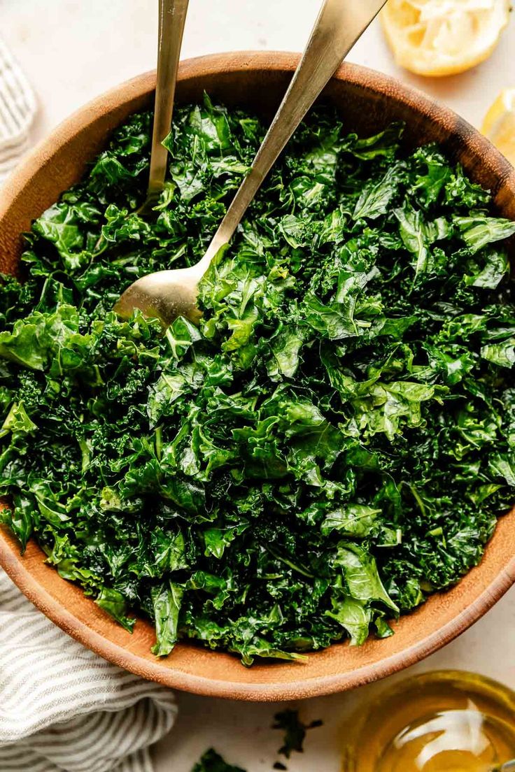 a wooden bowl filled with green leafy greens and two spoons resting on the side