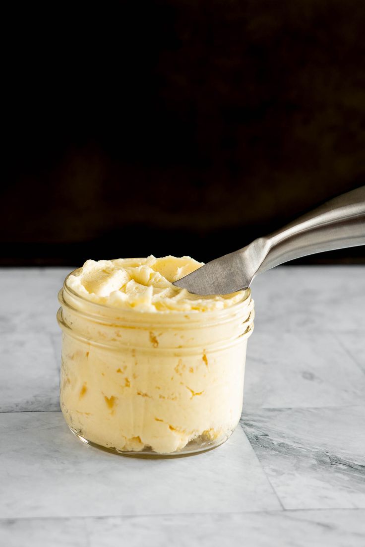 a jar filled with whipped cream on top of a marble counter next to a spoon