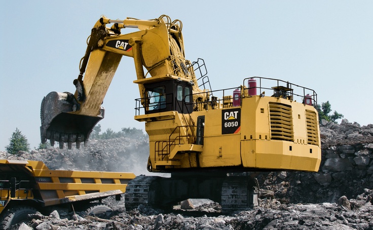 an excavator digging through rubble in front of a pile of rocks and trees