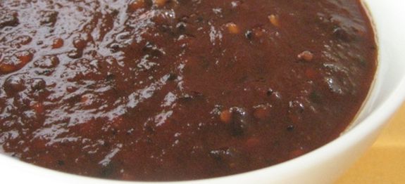 a white bowl filled with chili sauce on top of a wooden table next to an orange napkin