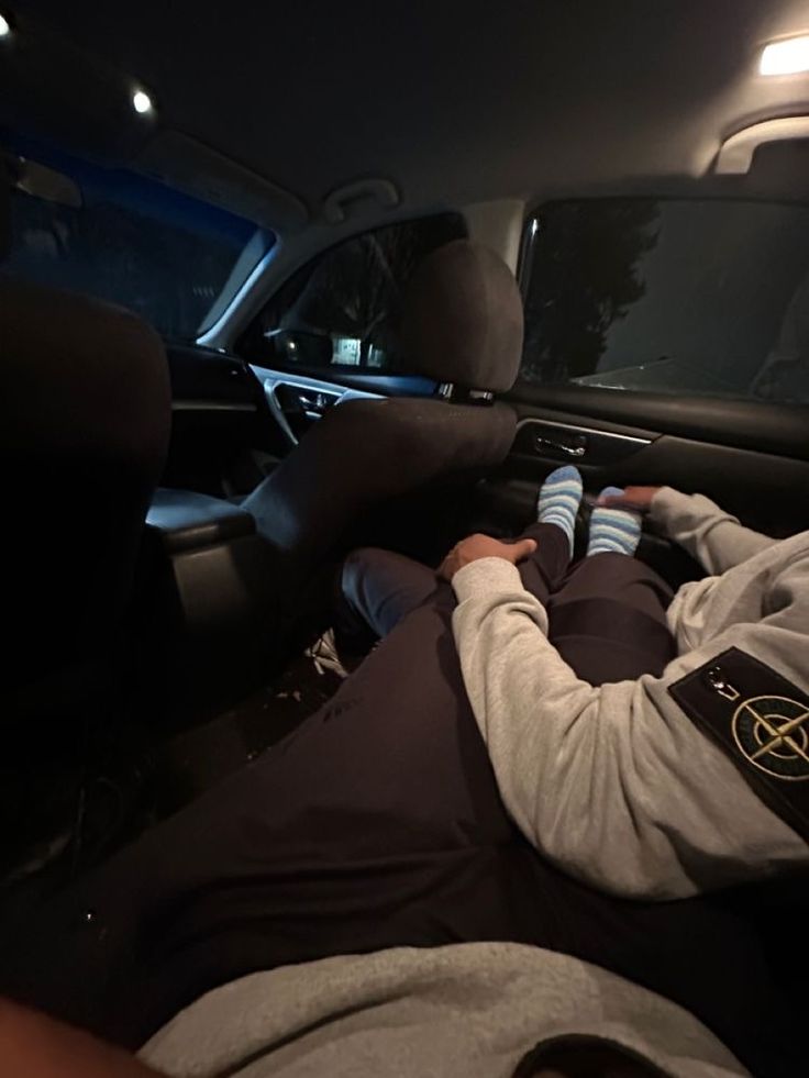 a man laying in the back seat of a car with his hands on the steering wheel