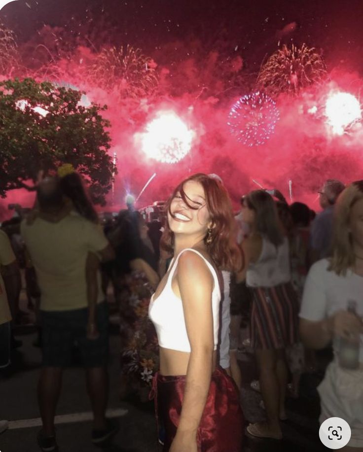 a woman standing in front of a crowd at night with fireworks on the sky behind her