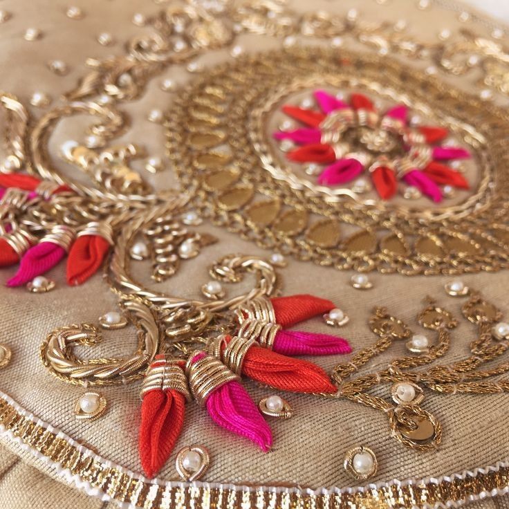 an embroidered pillow with red and pink tassels on it's edges, sitting on a table