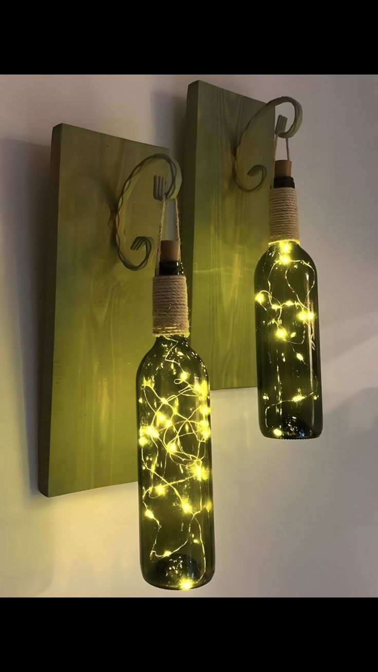 two bottles with lights in them hanging from hooks on the wall next to each other