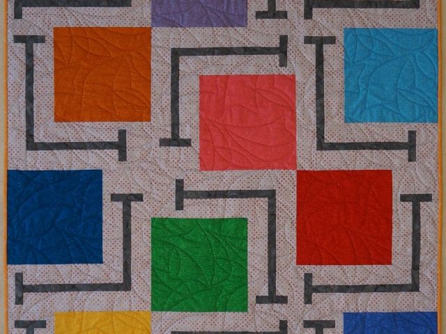 a multicolored quilt with squares and lines on the front is displayed in an orange frame