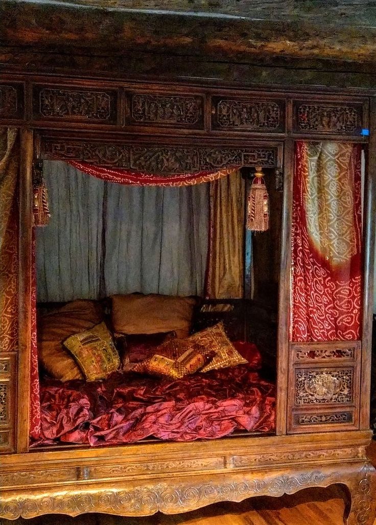 a bed that is in the middle of a room with red sheets and pillows on it