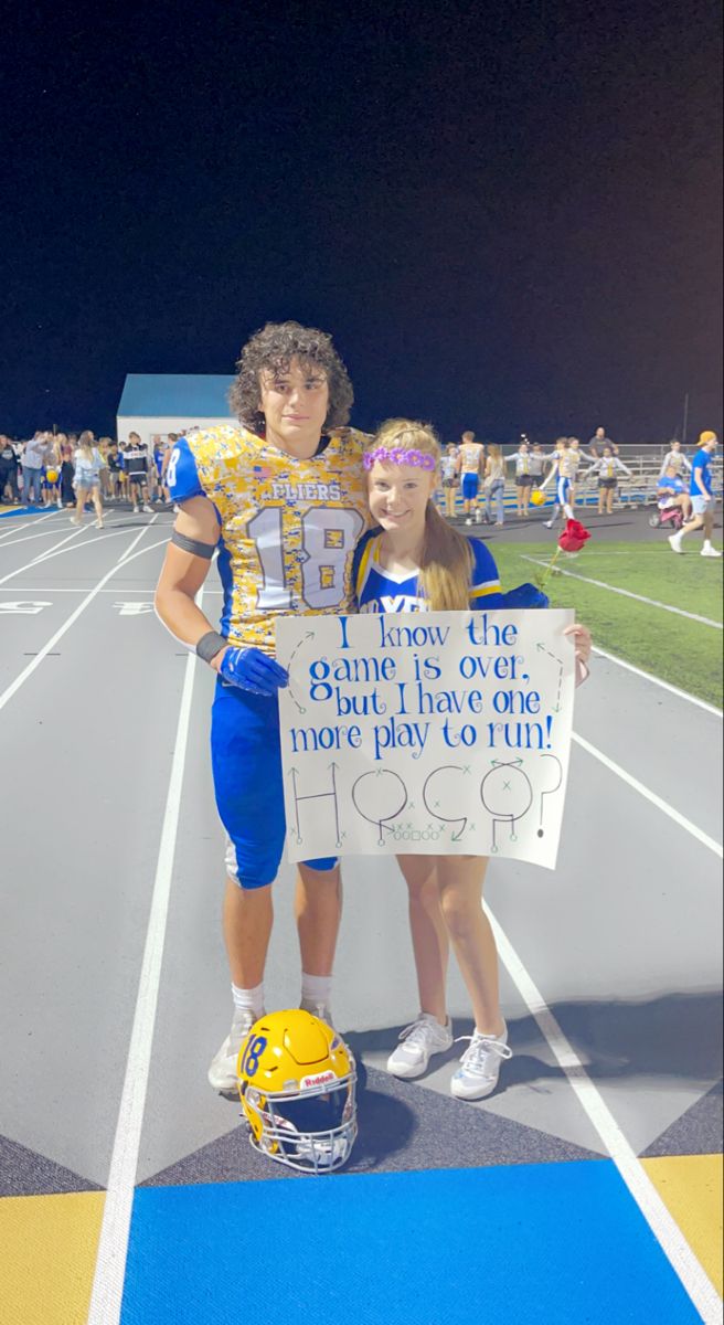 two people standing on a football field holding a sign