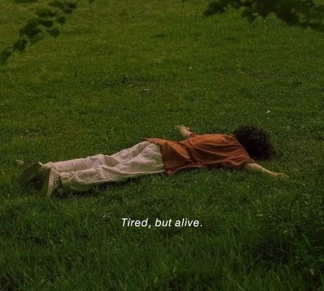 a person laying in the grass with their head on his back and there is a sign that says tired, but alive