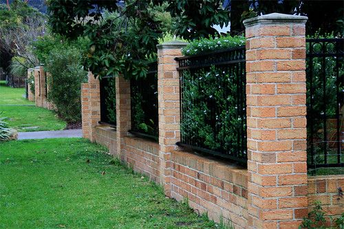 a brick fence with black iron bars on top and green grass in the foreground