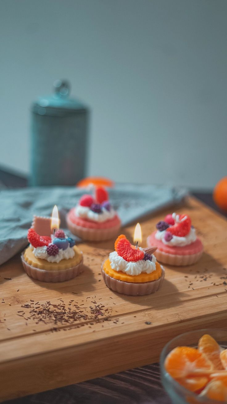 small cupcakes with candles on a wooden tray next to orange slices and other fruit