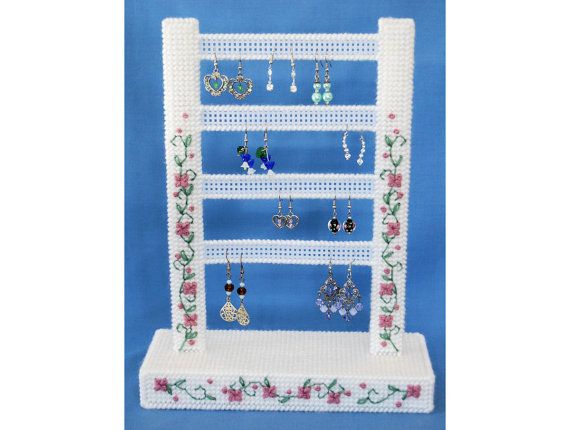 a crochet jewelry rack with earrings on it and flowers around the base, in front of a blue background