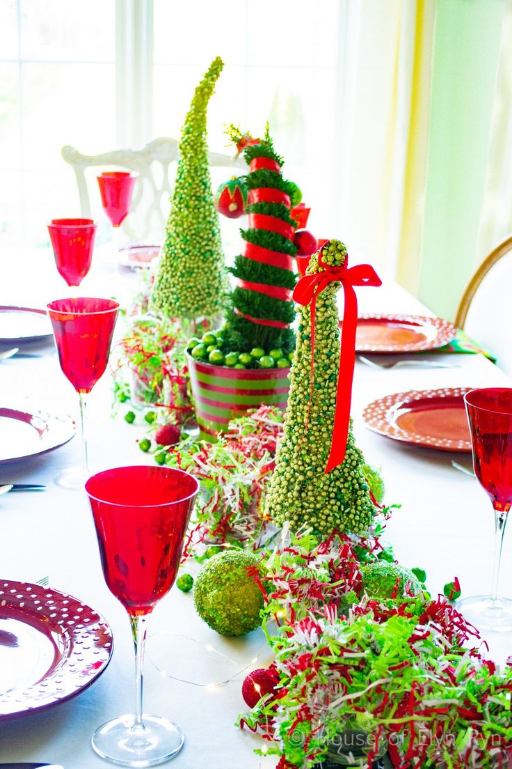 the table is set for christmas dinner with red wine glasses and green trees in pots