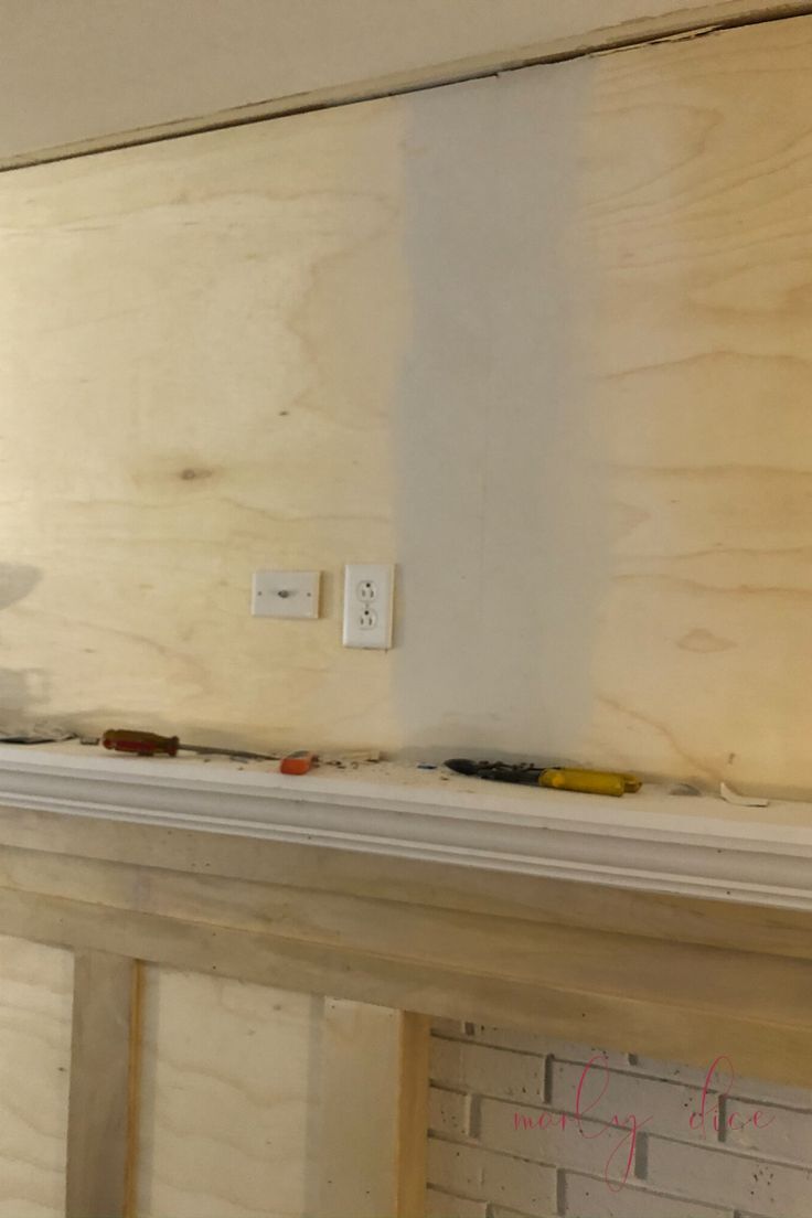 a man is painting the wall with white paint on top of a fireplace in an unfinished room