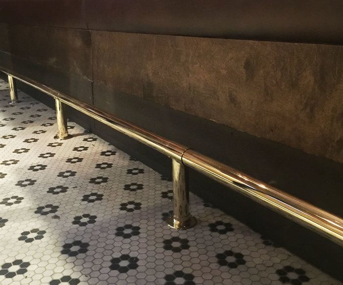 a long metal bench sitting on top of a tiled floor next to a wall with black and white tiles