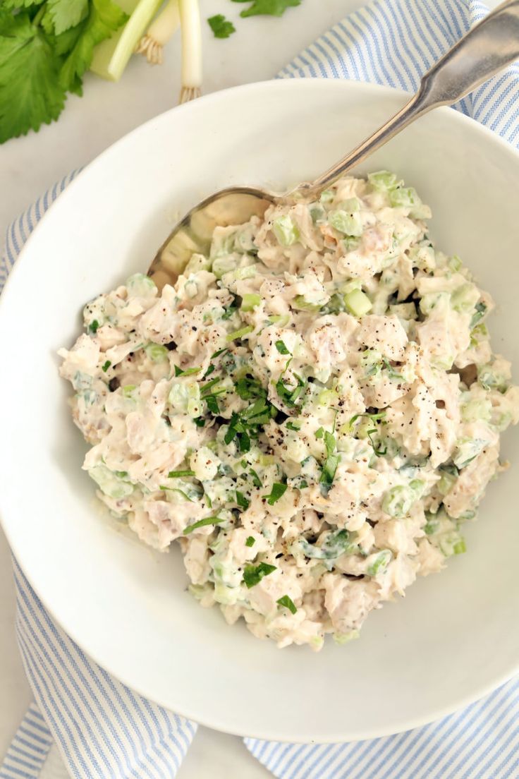 a white bowl filled with chicken salad next to celery