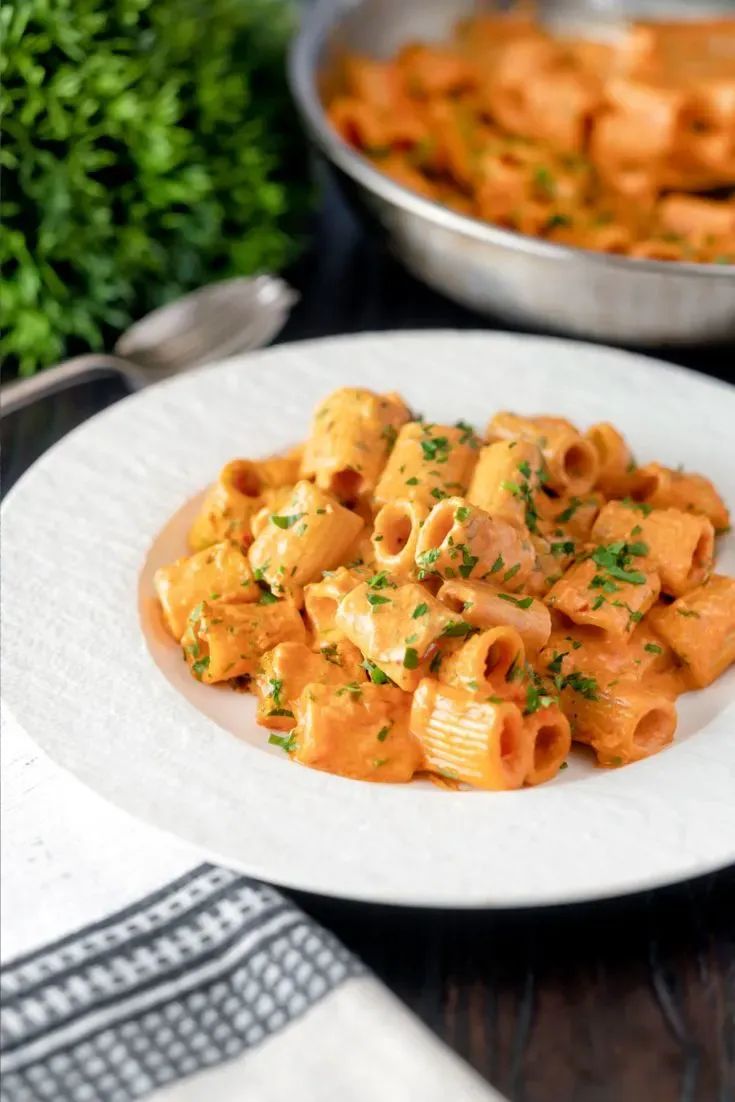 a white plate topped with pasta next to a bowl of carrots and parsley