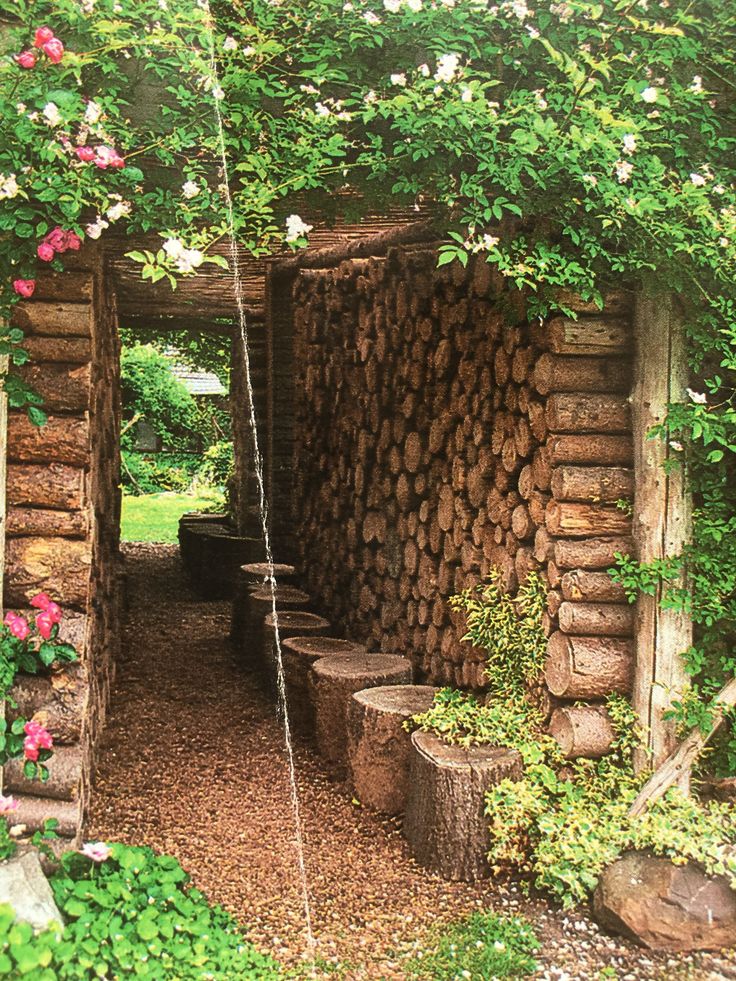 an outdoor area with logs and flowers growing on the walls, along with benches in the foreground