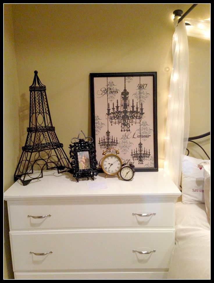 a white dresser topped with a clock next to a framed picture and a small eiffel tower