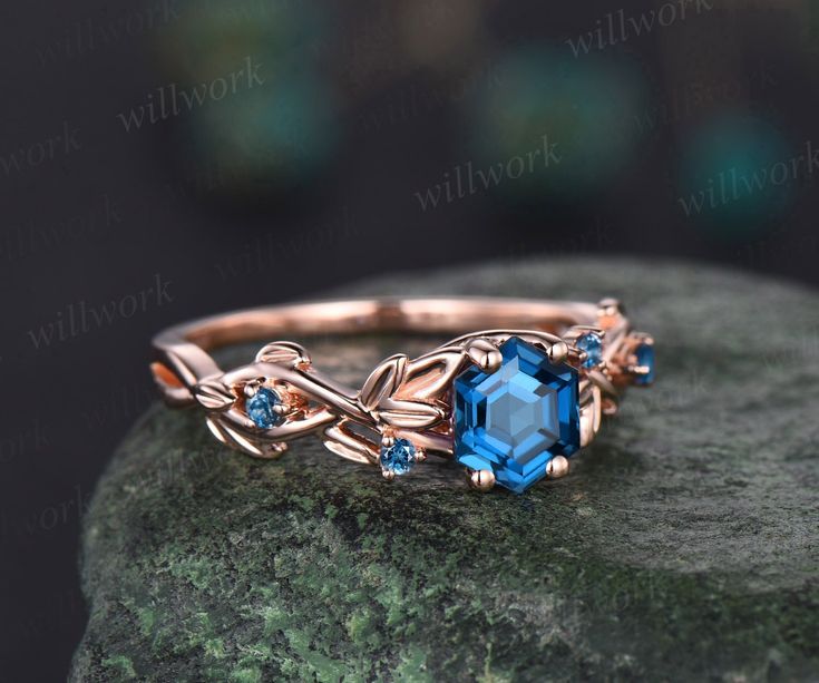 a gold ring with blue topazte and leaves on it sitting on a rock