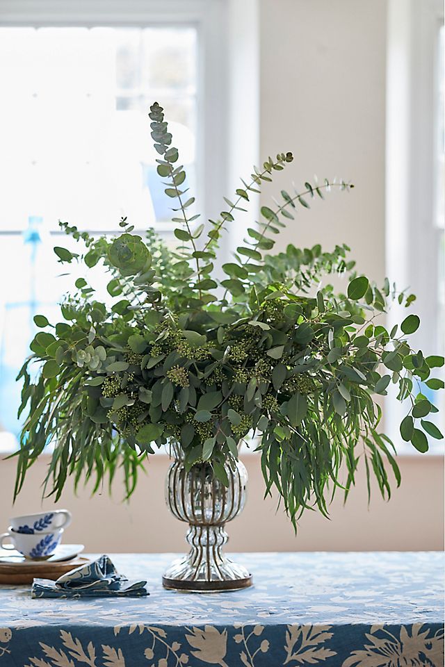 a vase filled with lots of green plants on top of a blue and white table cloth