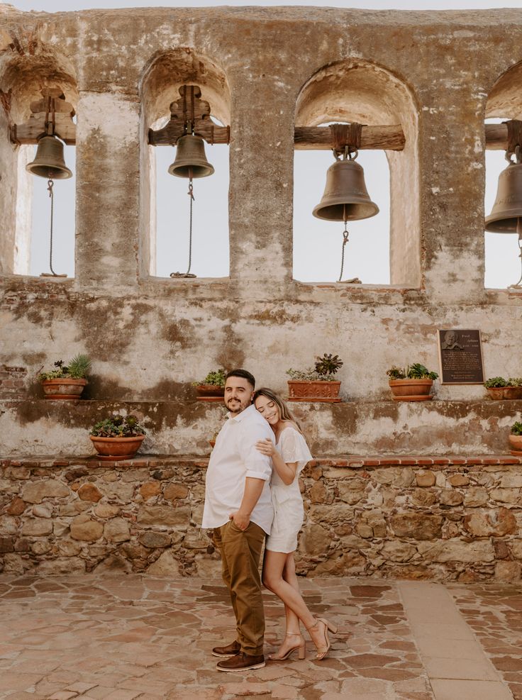 a man and woman standing next to each other in front of some bells on the wall