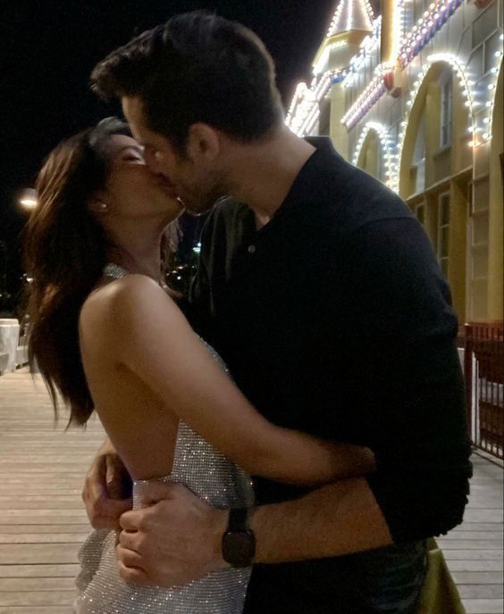 a man and woman kissing on a boardwalk at night