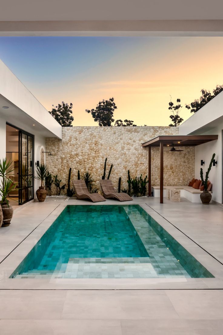 an empty swimming pool in front of a stone wall with plants and potted cacti