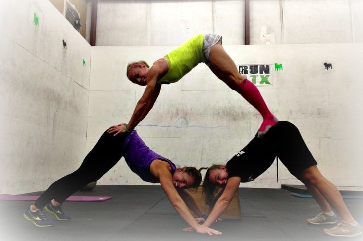 a man and woman doing yoga in a room with white walls, one holding the other upside down