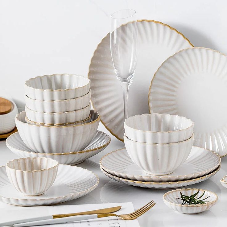 a table topped with white plates and gold trimmings next to utensils